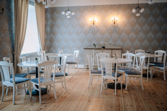 Elegant café or restaurant interior with white wooden chairs, round tables, vintage wallpaper, and warm lighting, creating a cozy and stylish atmosphere..