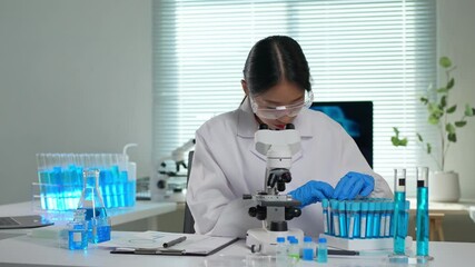 Professional female scientist in laboratory analyzing blue liquid in test tubes, performing experiments and taking notes, surrounded by scientific equipment