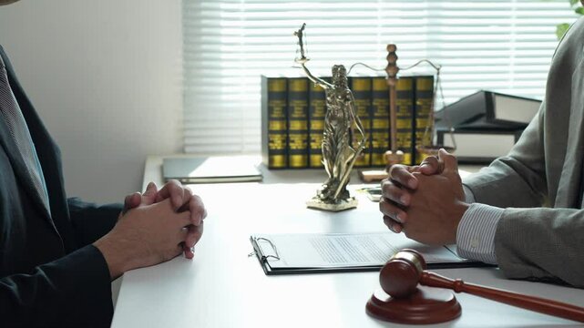 Legal professionals review and discuss contract terms, negotiating points of agreement in a formal office setting, with a gavel and themis statue symbolizing justice and law