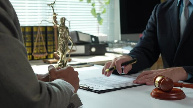 Professional lawyer guiding client through document signing, legal statuette and court hammer visible on polished desk surface, representing precise legal consultation and advisory process