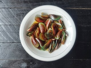 Stir-fried green mussels on plate with black wooden table background background. Flat lay
