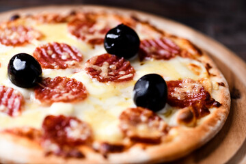 Pizza with salami, mozzarella and cheddar cheese. Wooden background. Soft focus. Close up.	