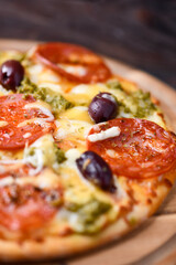 Pizza with chorizo ​​sausage, mozzarella and cheddar cheese, olive pesto and kalamata olives. Wooden background. Soft focus. Close up.	