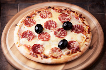 Pizza with salami, mozzarella and cheddar cheese. Wooden background. Soft focus. Close up.