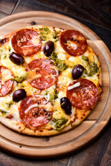 Pizza with chorizo ​​sausage, mozzarella and cheddar cheese, olive pesto and kalamata olives. Wooden background. Soft focus. Close up.