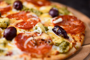 Pizza with chorizo ​​sausage, mozzarella and cheddar cheese, olive pesto and kalamata olives. Wooden background. Soft focus. Close up.