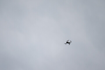 A low-angle shot of a drone flying in a gray sky. The drone is small compared to the vastness of the sky, giving a sense of scale.