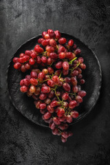 An elegant bunch of red fresh grapes on a black textured plate on a black textured background. Flat lay. Top veiw.