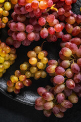 Close-up of red and yellow grapes on a dark textured plate with soft lighting and a dark background