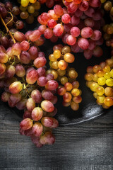 Fresh red yellow grapes on a dark textured plate with soft lighting and rich color contrast against a dark gray wooden background