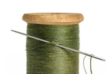 Old Single wooden spool of thread olive green color and needle closeup white background