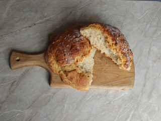Homemade round white bread on the wooden cutting board, lying on the marble table. Advert for bakery, cafe and restaurants. Horizontal.