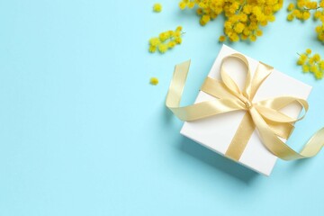Beautiful composition with spring mimosa branches and gift box on a colored background
