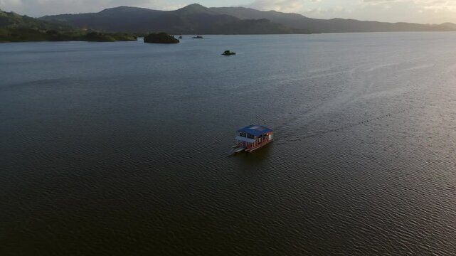 Ferry boat with tourist on water reserve of Hatillo Dam at sunset time. Aerial orbit shot. Beautiful landscape in Dominican Republic. Wide shot.