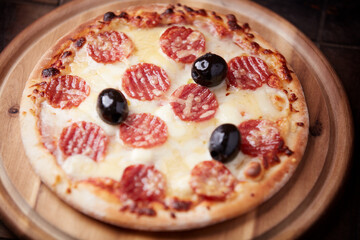Pizza with salami, mozzarella and cheddar cheese. Wooden background. Soft focus. Close up.