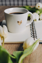 Cup of Coffee, open book and a bouquet  tulip flowers over  wood table top.  Composition with copy space. 
 Minimal flower arrangement.