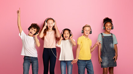Obraz premium Multiethnic schoolchildren in headphones listening to music or audio books on pink background