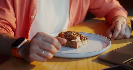 A stylishly dressed man uses a laptop while sitting at a table in a cafe, a close-up of men's hands, no face