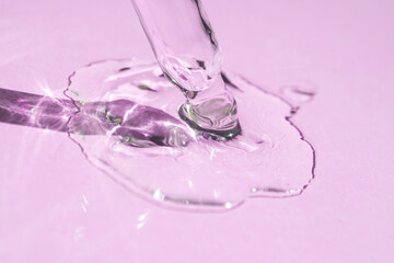 A drop of oil or gel falls from a cosmetic dropper on a pink background.