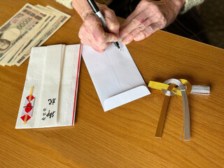 祝儀袋の横で封筒に記述する高齢女性の手元