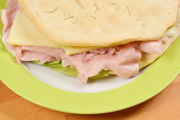 A close-up shot of a sandwich on a green plate reveals a simple filling of ham, cheese, and lettuce, emphasizing the fresh ingredients and light meal