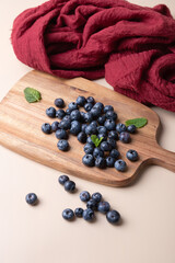 Fresh blueberries on wooden board with mint leaves and red fabric on beige background. Natural and rustic style. Concept of healthy eating, freshness and home cooking