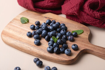 Blueberries scattered on wooden board with mint and red fabric on neutral background. Warm and natural styling. Concept of freshness, healthy eating and home cooking