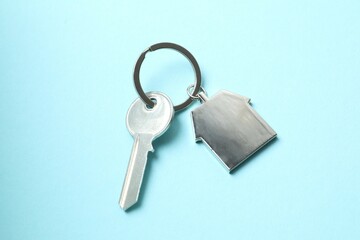 Metallic key with keychain in shape of house on color background
