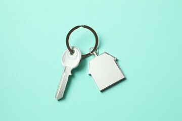 Metallic key with keychain in shape of house on color background