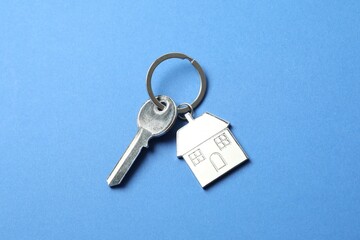 Metallic key with keychain in shape of house on color background