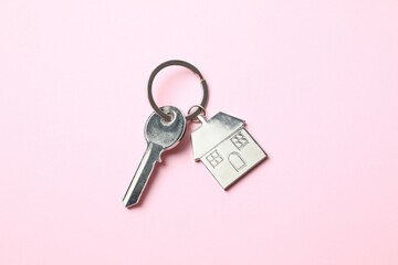 Metallic key with keychain in shape of house on color background