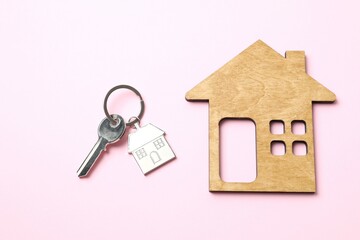 Metallic key with keychain and wooden house on color background