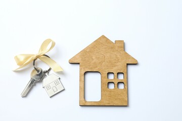 Metallic key with keychain and wooden house on white background