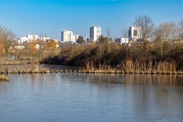 Obraz premium Partially frozen pond with an urban skyline backdrop on a clear winter day