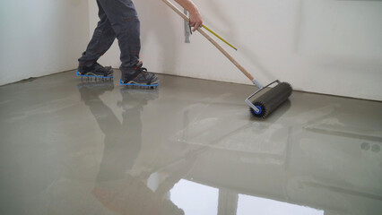 Construction worker leveling concrete using a spike roller on a self-leveling floor