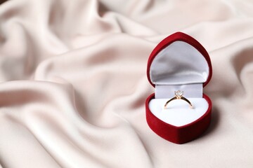 Beautiful shiny gold engagement ring with large diamond gemstone in a rich red velvet box on silk...