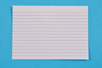 A top-down shot of a single white, ruled index card with a red line at the top, placed against a blue background