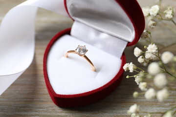 Beautiful shiny gold engagement ring with large diamond gemstone in a rich red velvet box on wooden background
