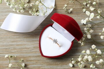 Beautiful shiny gold engagement ring with large diamond gemstone in a rich red velvet box on wooden...