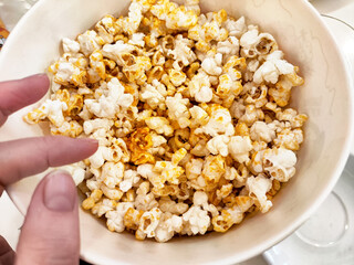Freshly popped popcorn in a large bowl with a hand reaching in for a snack