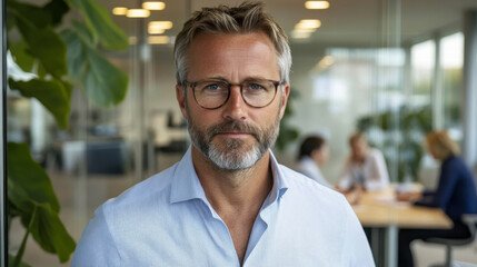 Obraz premium confident man with glasses and beard stands in modern office environment, exuding professionalism and focus