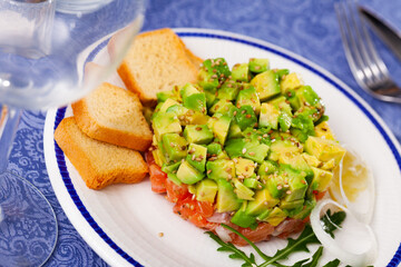 Gourmet salmon tartare with chopped avocado and toasted bread served on white plate