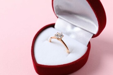 Beautiful shiny gold engagement ring with large diamond gemstone in a rich red velvet box on color...