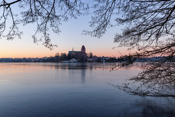 Doem of Ratzeburg at a beautiful winter morning with ice covered lake, framed by branches and twigs, Schleswig-Holstein, Northern Germany