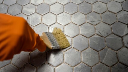 Construction worker applying grout on hexagonal tiles with brush