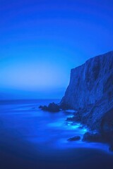 Calm ocean waves gently lap against dramatic blue cliff under tw