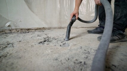 Construction worker using a powerful industrial vacuum cleaner to remove dust and debris from a...
