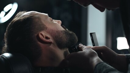 Skilled barber grooming client's beard using electric razor, delivering precise styling within...