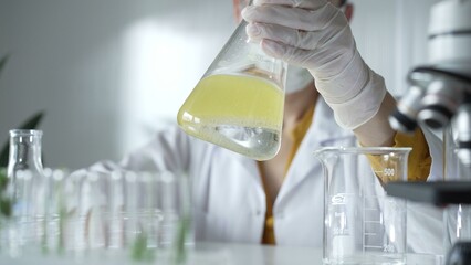 A scientist wearing white protective gloves is shaking up a yellow chemical solution inside an...