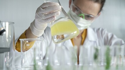 A scientist wearing white protective gloves is shaking up a yellow chemical solution inside an...